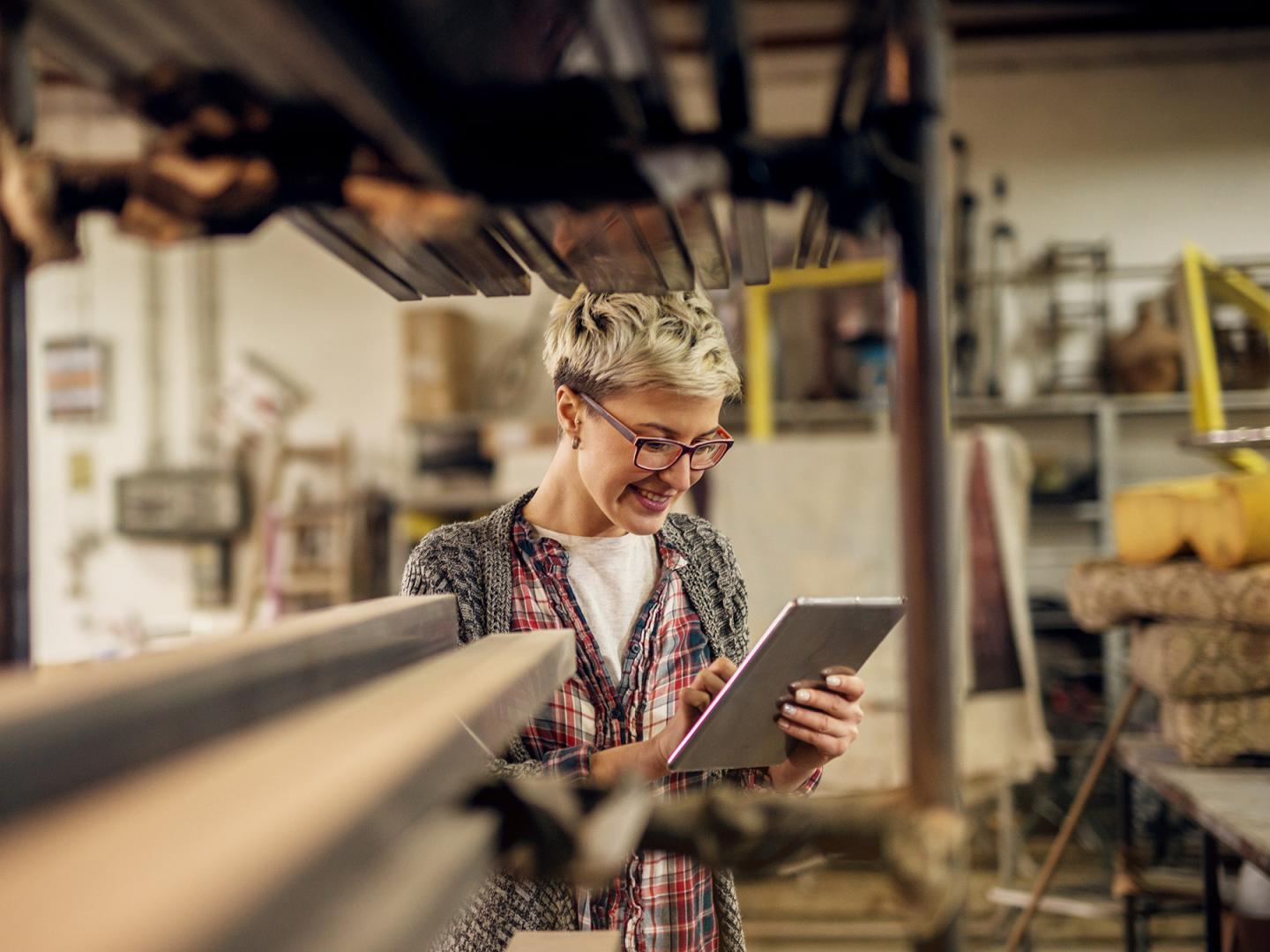 Junge Frau in der Werkstatt bedient ein Tablet.