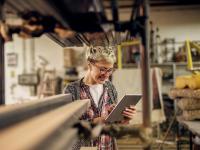 Junge Frau in der Werkstatt bedient ein Tablet.