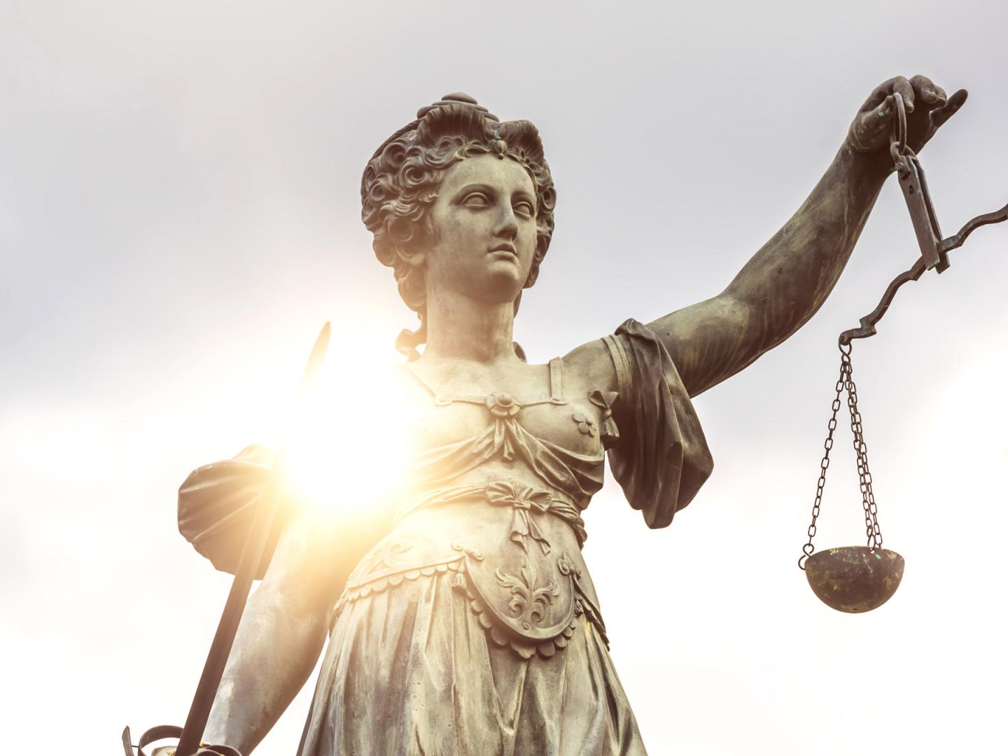 Eine Statue der Justitia wird von der Sonne angestrahlt.