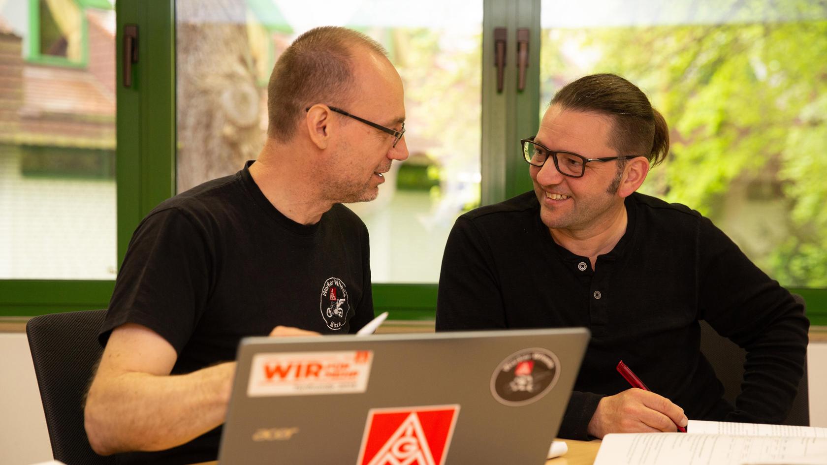 Zwei Beschäftigte sitzen an einem Tisch vor einem Laptop