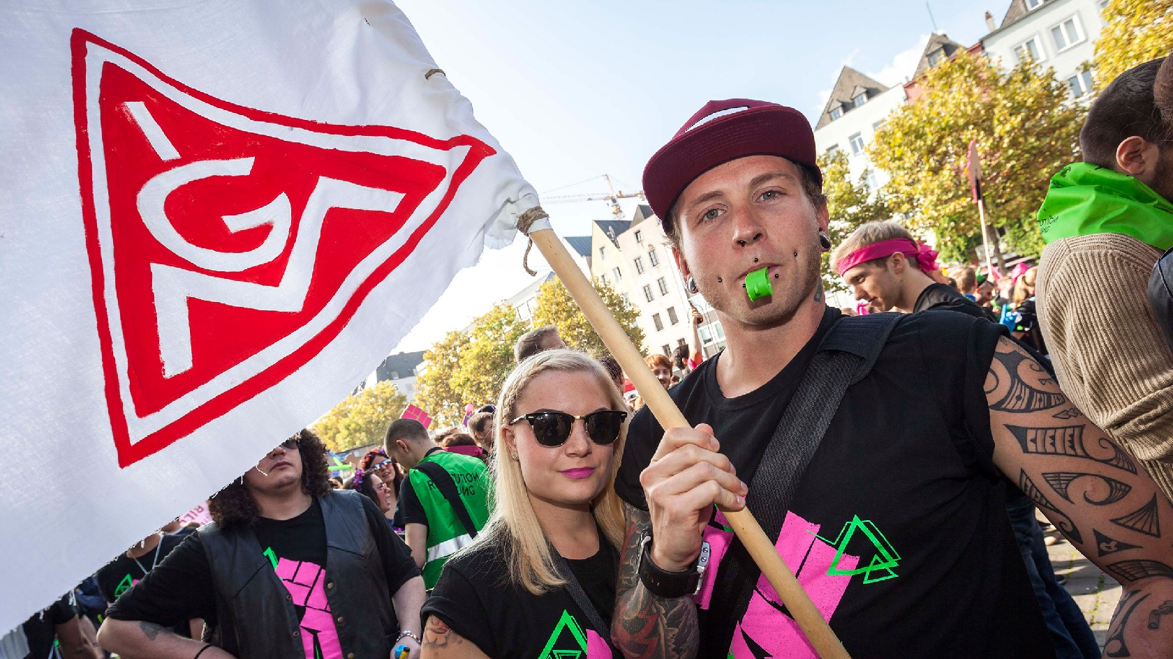 Junge Frau und junger Mann schwenken auf einer Demo die IG-Metall-Fahne.