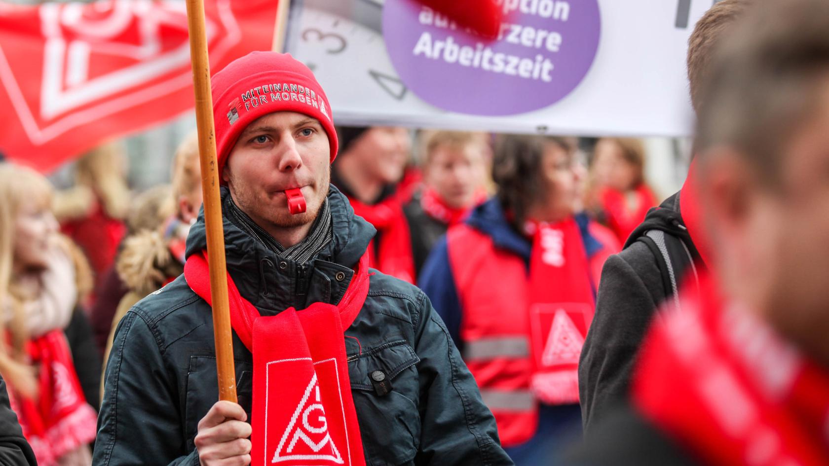 Junger Mann mit Transparent, Pfeife und IG Metall-Schal auf einer Demo.