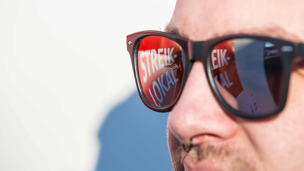 Junger Mann mit Sonnenbrille, in der sich das Wort Streiklokal spiegelt.