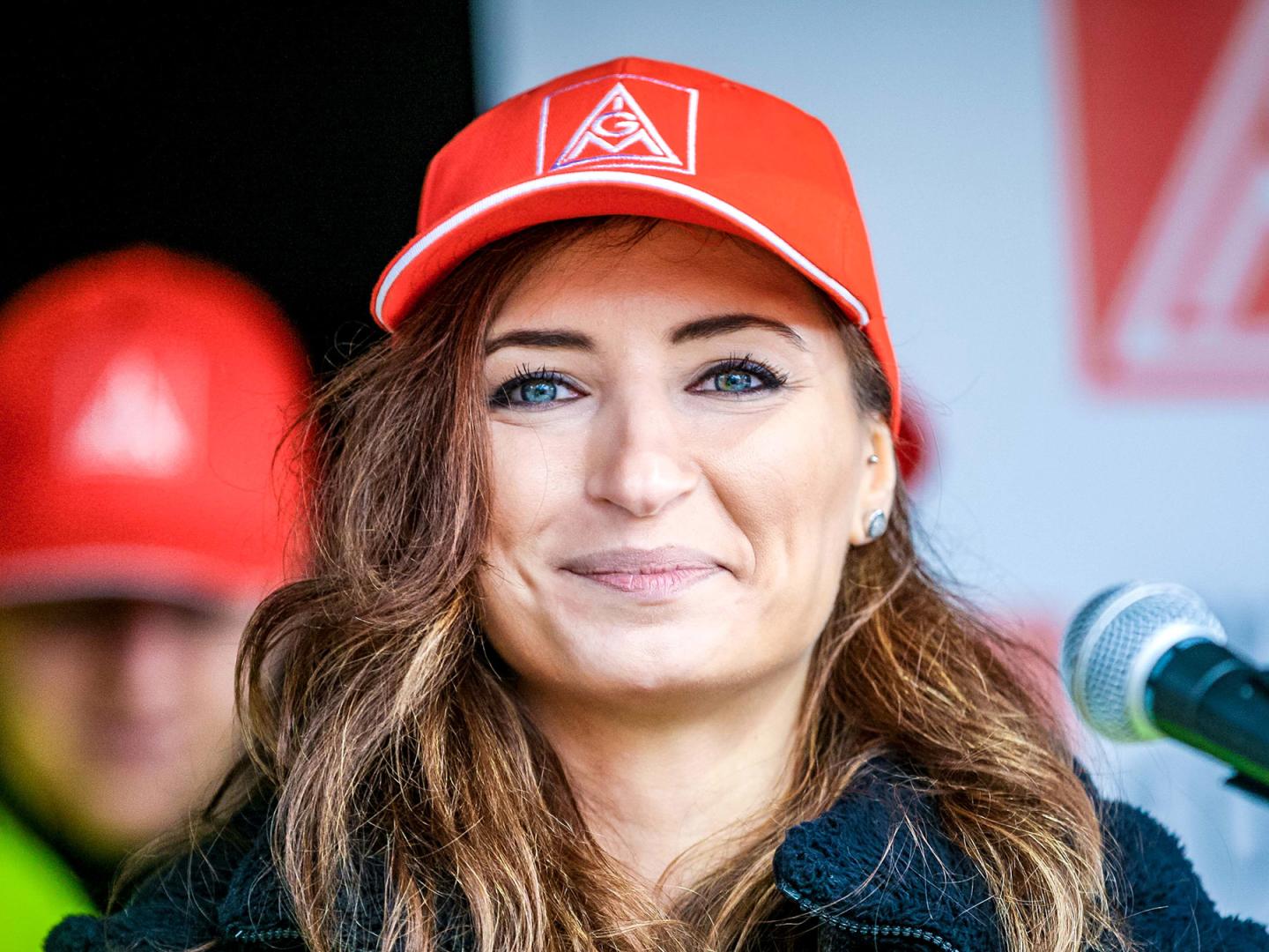 Eine Frau mit langem braunem Haar und IG Metall-Kappe blickt lächelnd in die Kamera.
