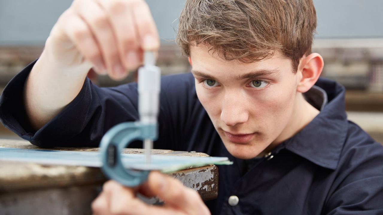 Junger Mann misst mit einem Feinmessgerät eine Metallplatte aus.