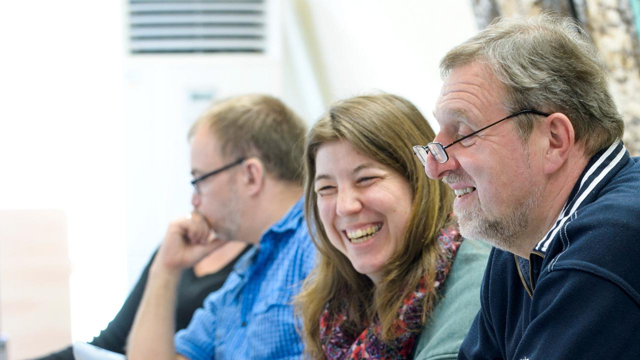 Drei ältere Männer und eine Frau lachend während eines Seminars.