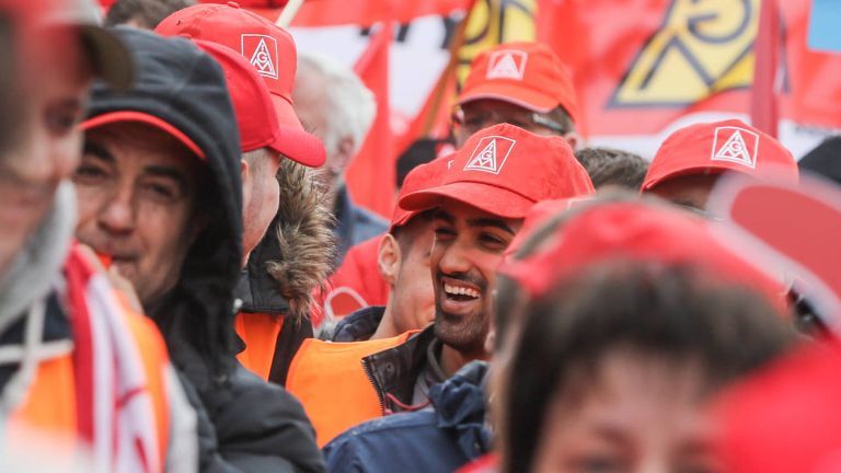 Ein lachender Mann mit IG Metall-Kappe in einer Menschenmenge.