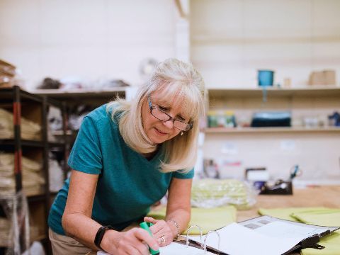 Eine Frau in einer Werkstatt beugt sich über einen Aktenordner und notiert etwas.