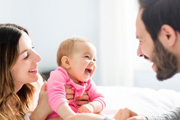 Mutter, Vater und Kind liegen auf einem weißen Bett