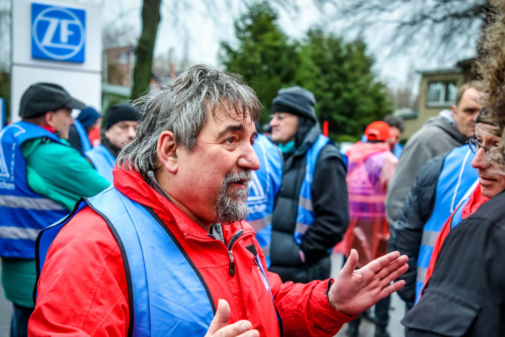Ein Mann in einer blauen Streikeste im Gespr&auml;ch mit einem anderen Mann.