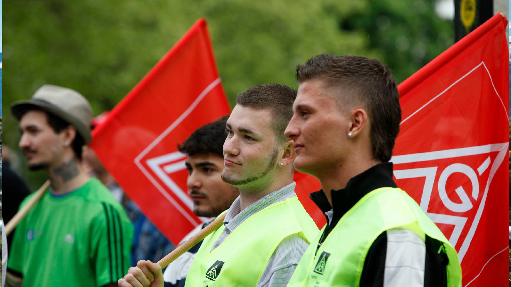 Drei junge Männer mit gelben Warnwesten und IG Metall-Fahnen über der Schulter.