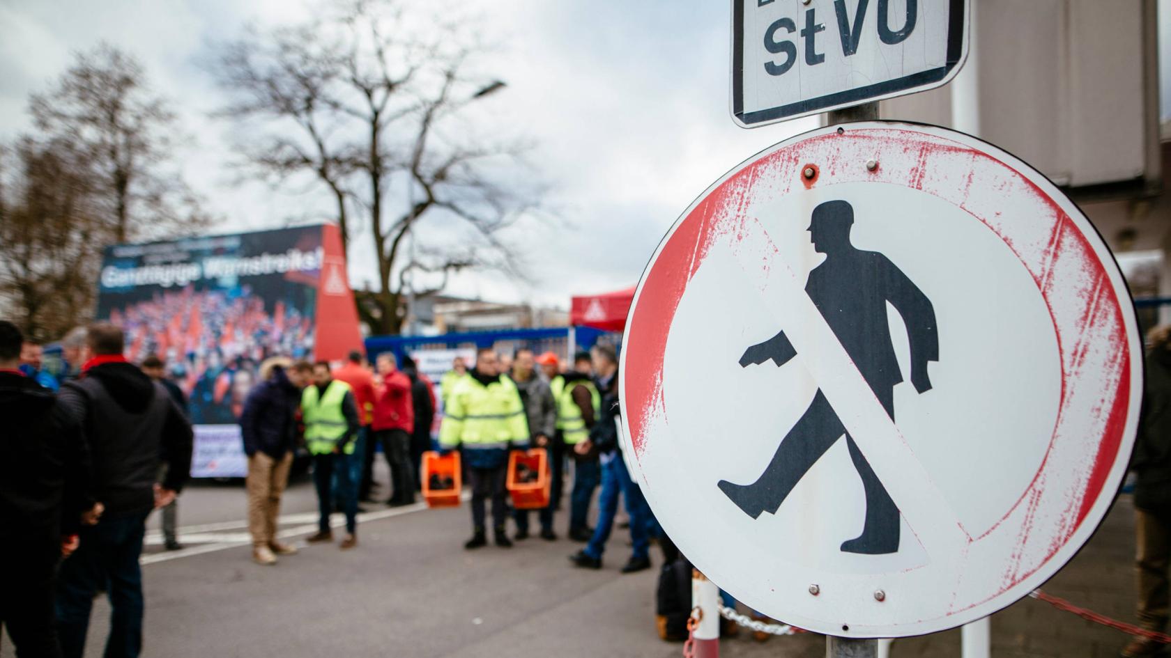 Ein Verkehrsschild im Vordergrund und eine Gruppe Streikende dahinter.