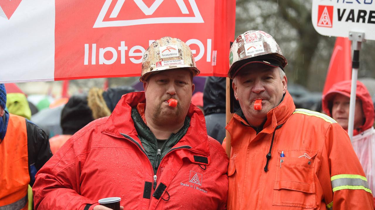 Zwei Männer mit Schutzhelmen und roten Trillerpfeifen im Mund blicken fröhlich in die Kamera.