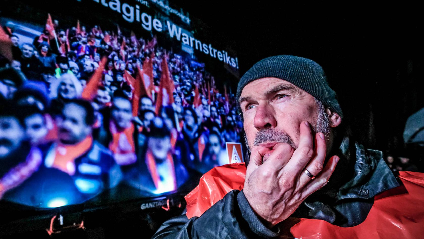 Ein Mann mit Mütze und Streikweste pfeift durch die Finger.