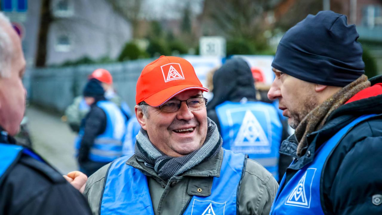 Ein Mann mit IG Metall-Kappe unterhält sich mit einem anderen Mann. 
