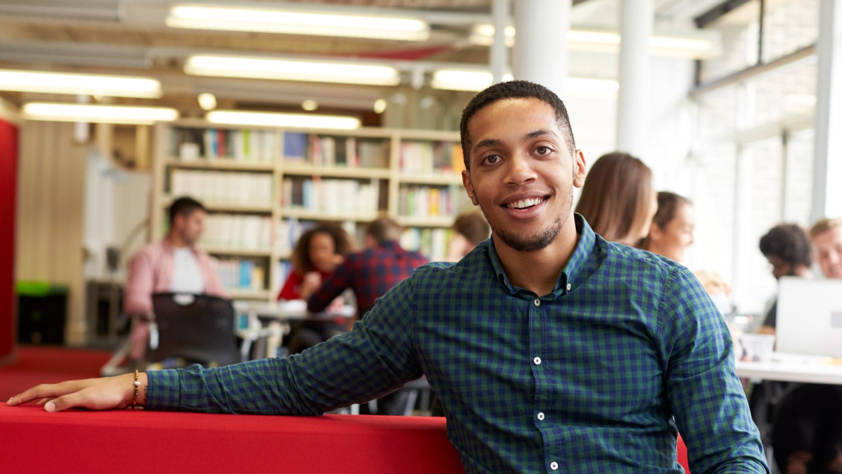 Student sitzt in der Bibliothek auf einem roten Sofa.