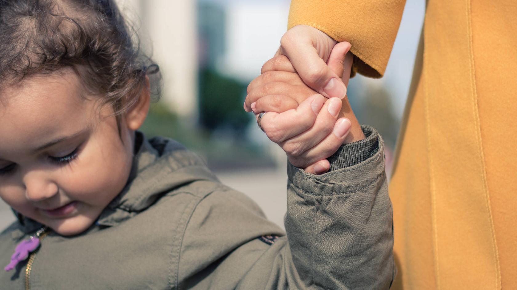Ein kleines Mädchen hält die Hand eines Erwachsenen.