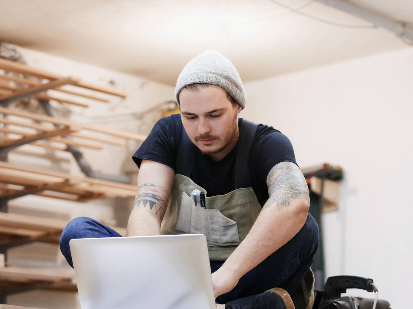 Ein junger Mann in einer Werkstatt blickt in ein Notebook.