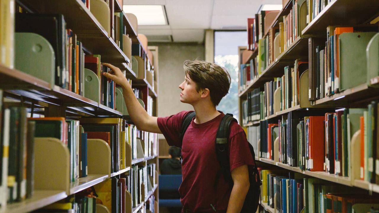 Ein junger Mann nimmt ein Buch aus einem Regal in einer Bibliothek.