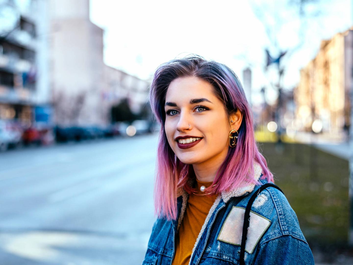 Eine junge Frau mit pinken Haaren lächelt in die Kamera.