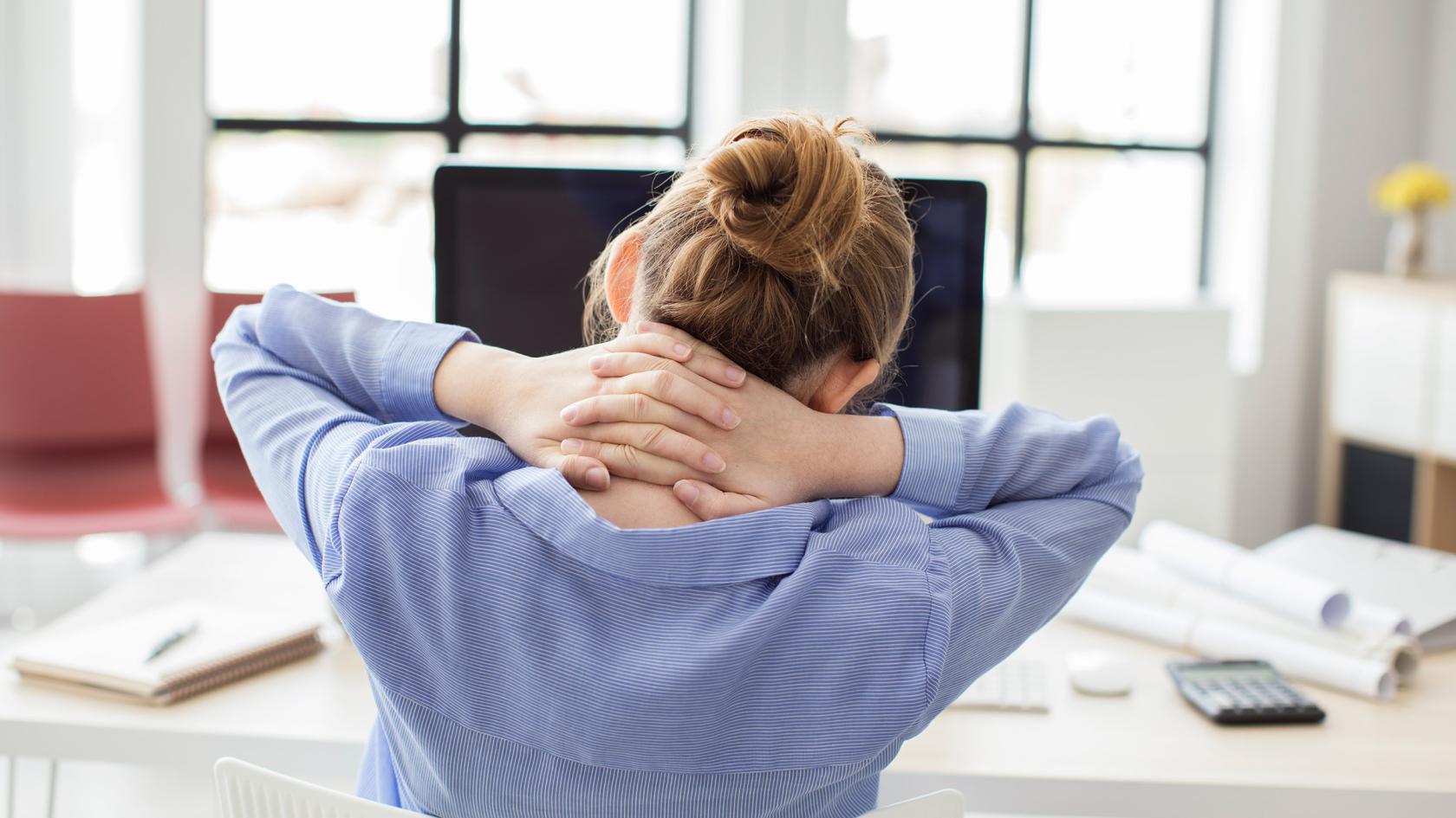 Eine Frau an einem Computerarbeitsplatz hat Nacken- und Rückenschmerzen