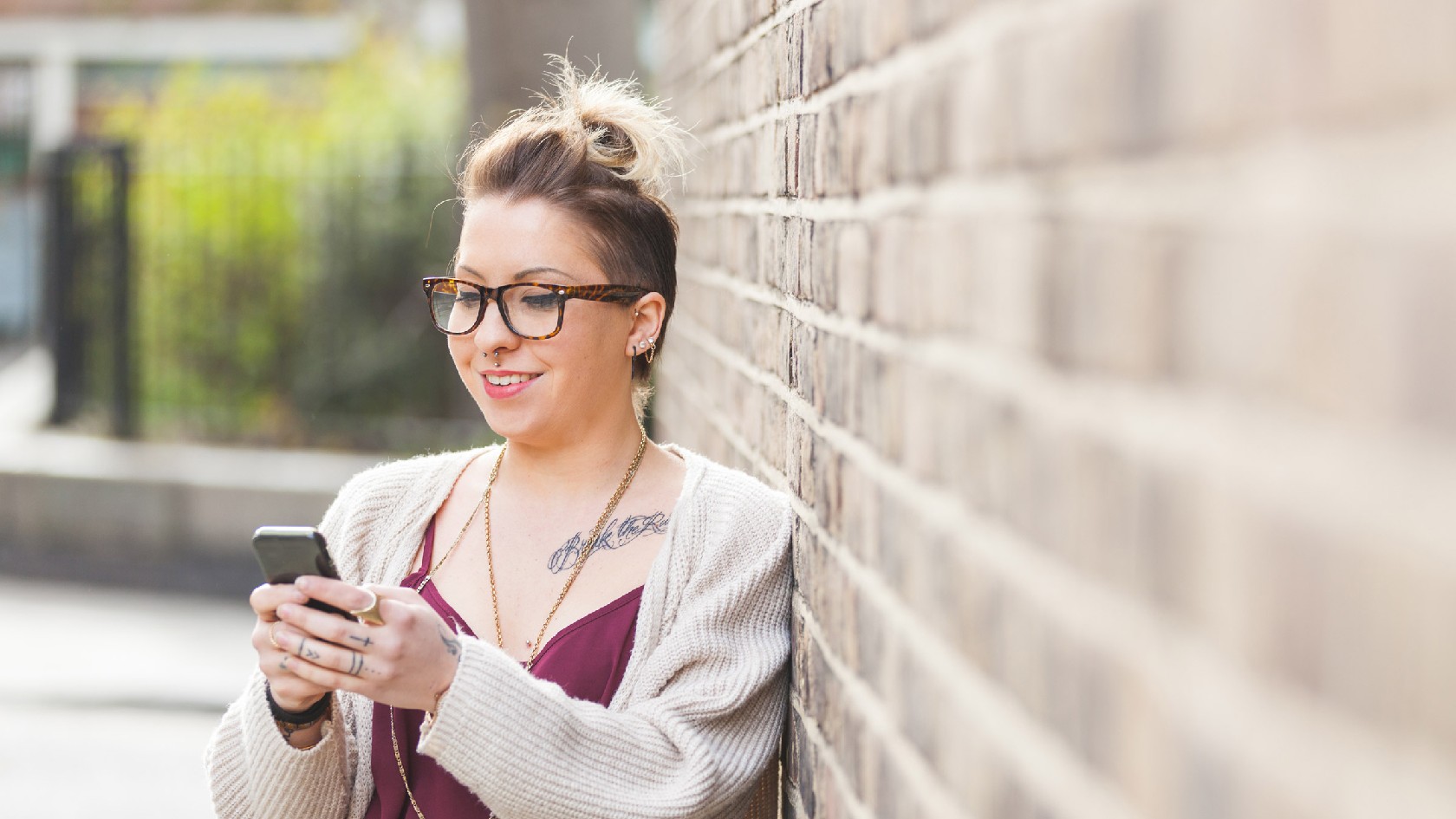 Junge Frau lehnt an einer Wand und tippt auf ihrem Handy.