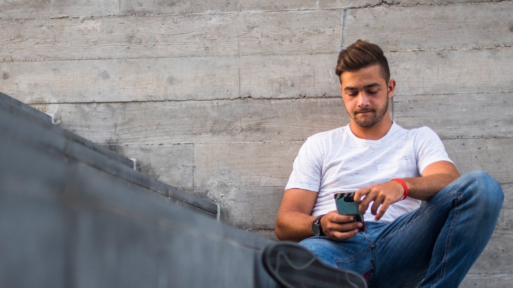 Junger Mann sitzt auf einer Treppe und tippt auf seinem Smartphone.