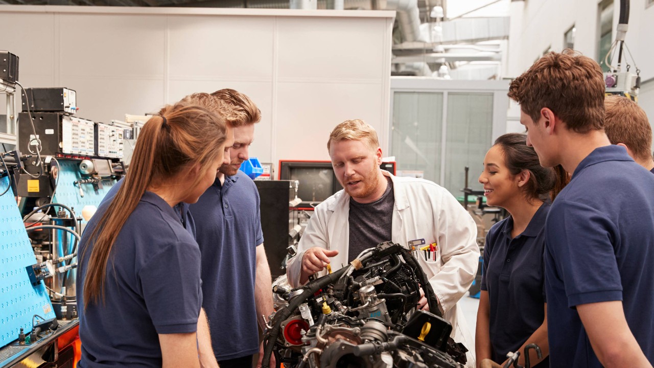 Auszubildende und Ausbilder stehen um einen Motor herum.