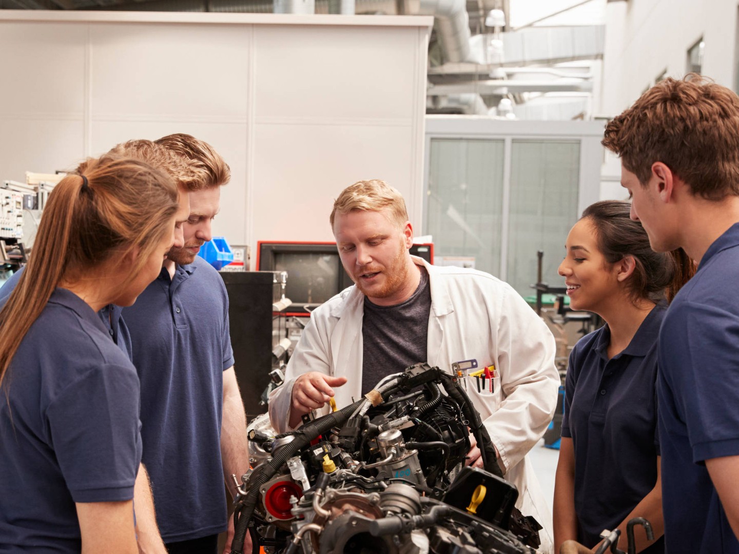 Auszubildende und Ausbilder stehen um einen Motor herum.