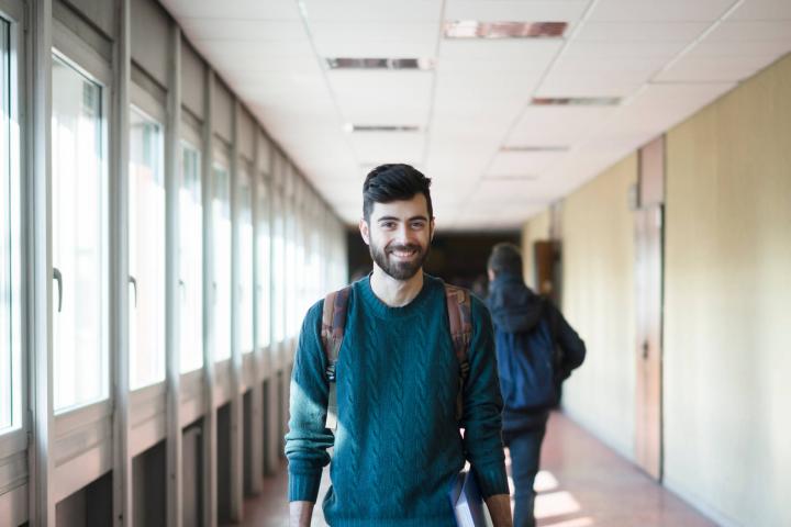 Ein junger Mann mit einem Ordner unter dem Arm geht durch einen Flur.