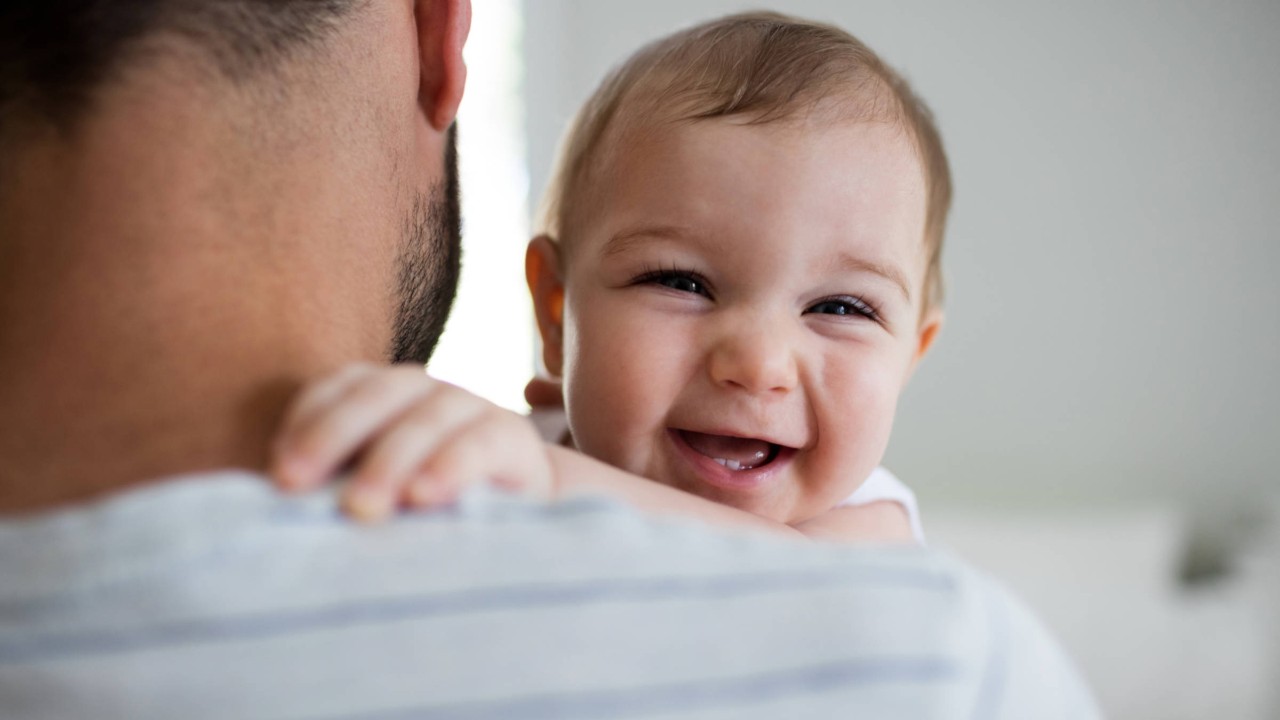 Ein lächelndes Baby auf dem Arm seines Vaters.