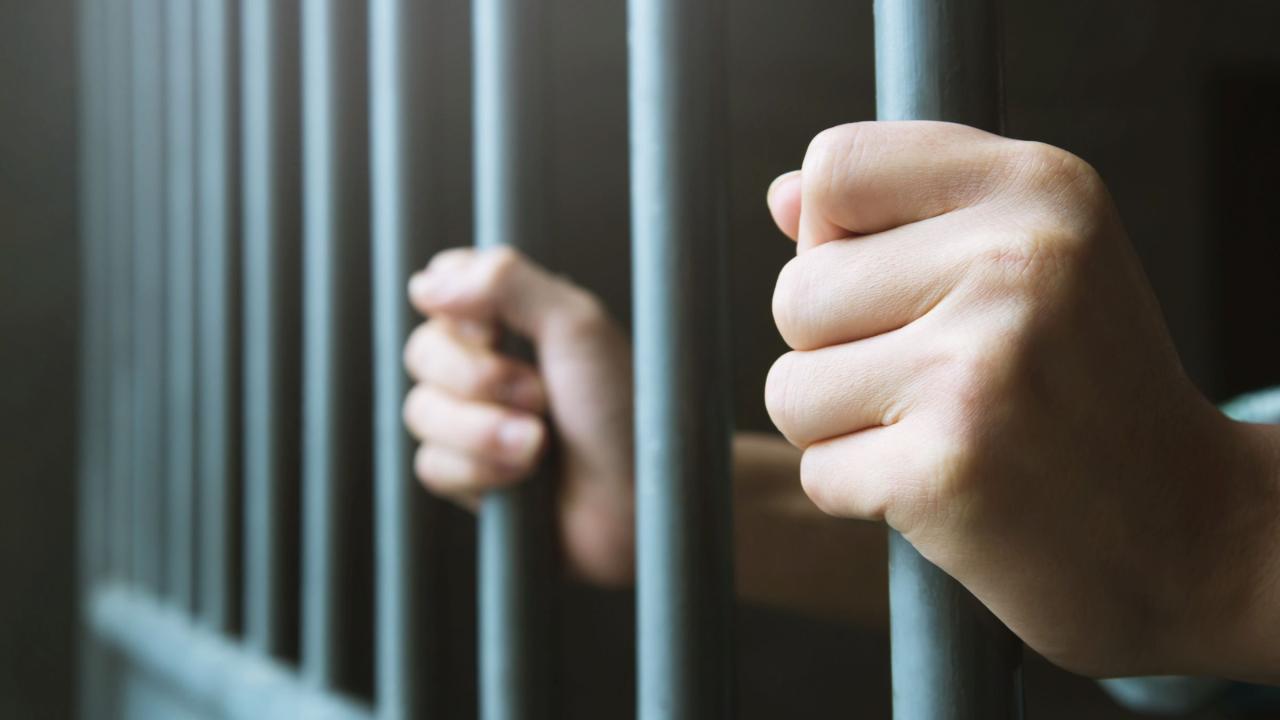 Hände klammern sich an Stangen einer Gefängniszelle