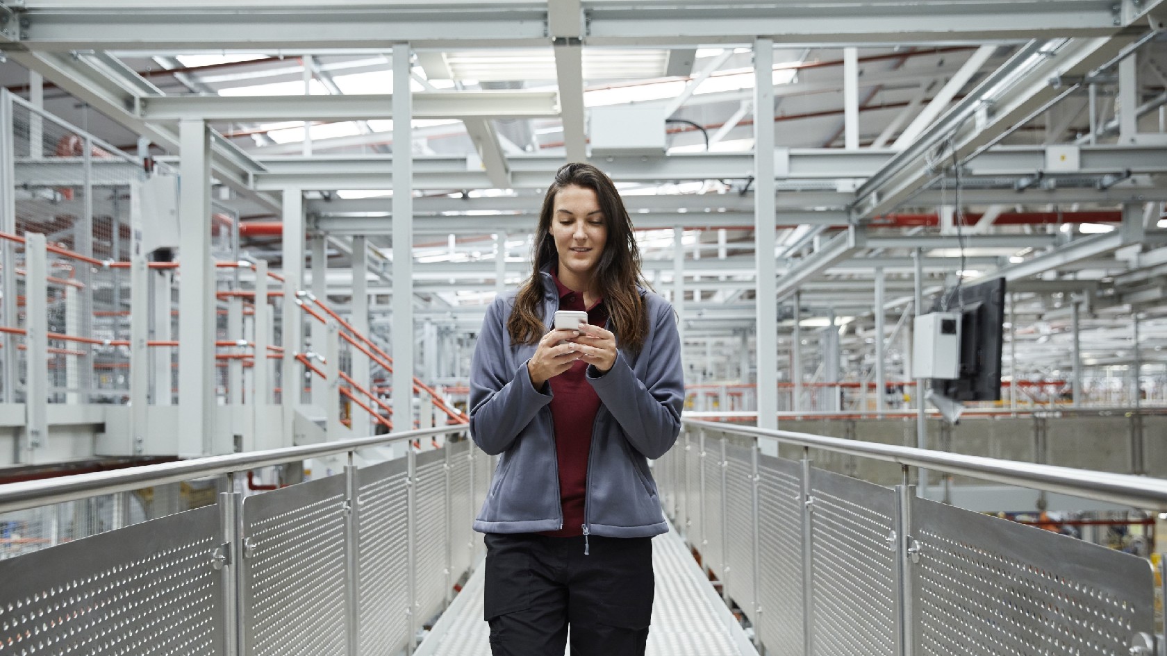 Eine junge Frau in Arbeitskleidung blickt auf ein Smartphone.