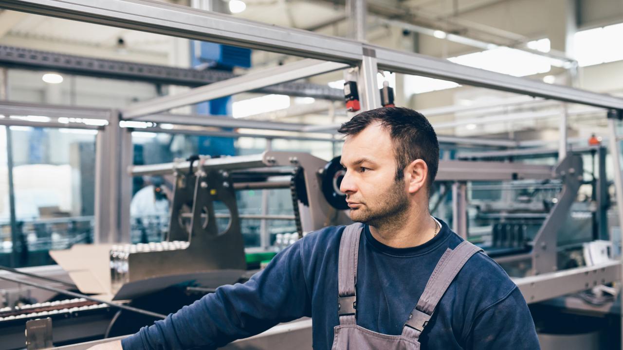 Mann steht an einer Maschine in einer Werkshalle