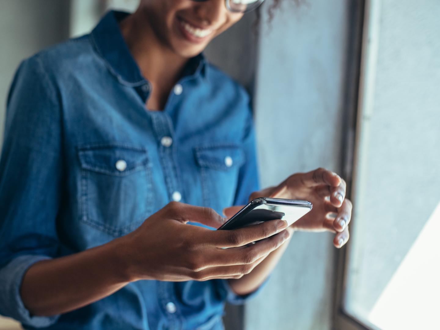 Eine junge Frau schaut lächelnd auf ihr Handy.