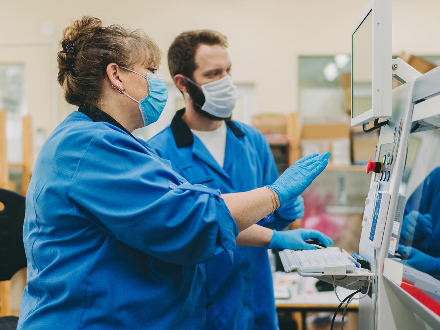 Arbeiter stehen mit einem Mundschutz vor einer Drehmaschine