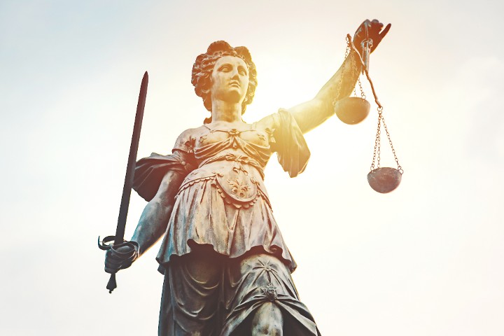 Statue von Justizia mit Schwert und Waage in der Hand vor blauem Himmel