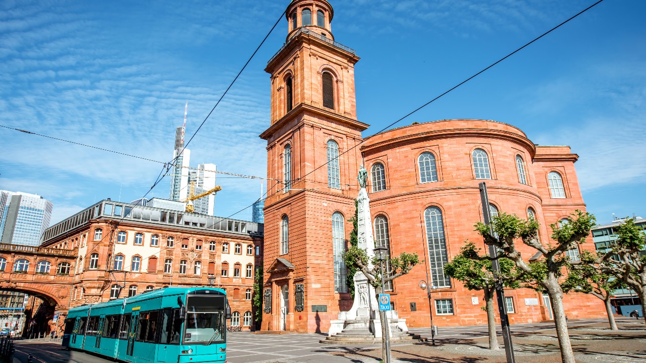 Paulskirche in Frankfurt am Main mit Tram davor und Skyline in Hintergrund.