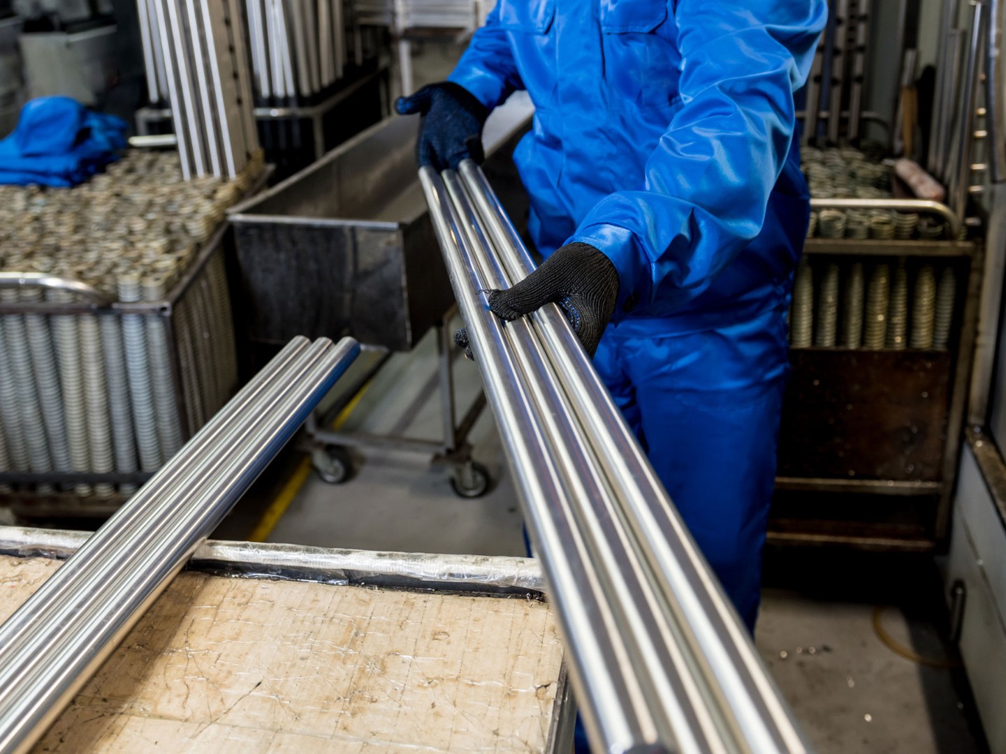 Ein Beschäftigter in einer Werkshalle hält Metallrohre in den Händen