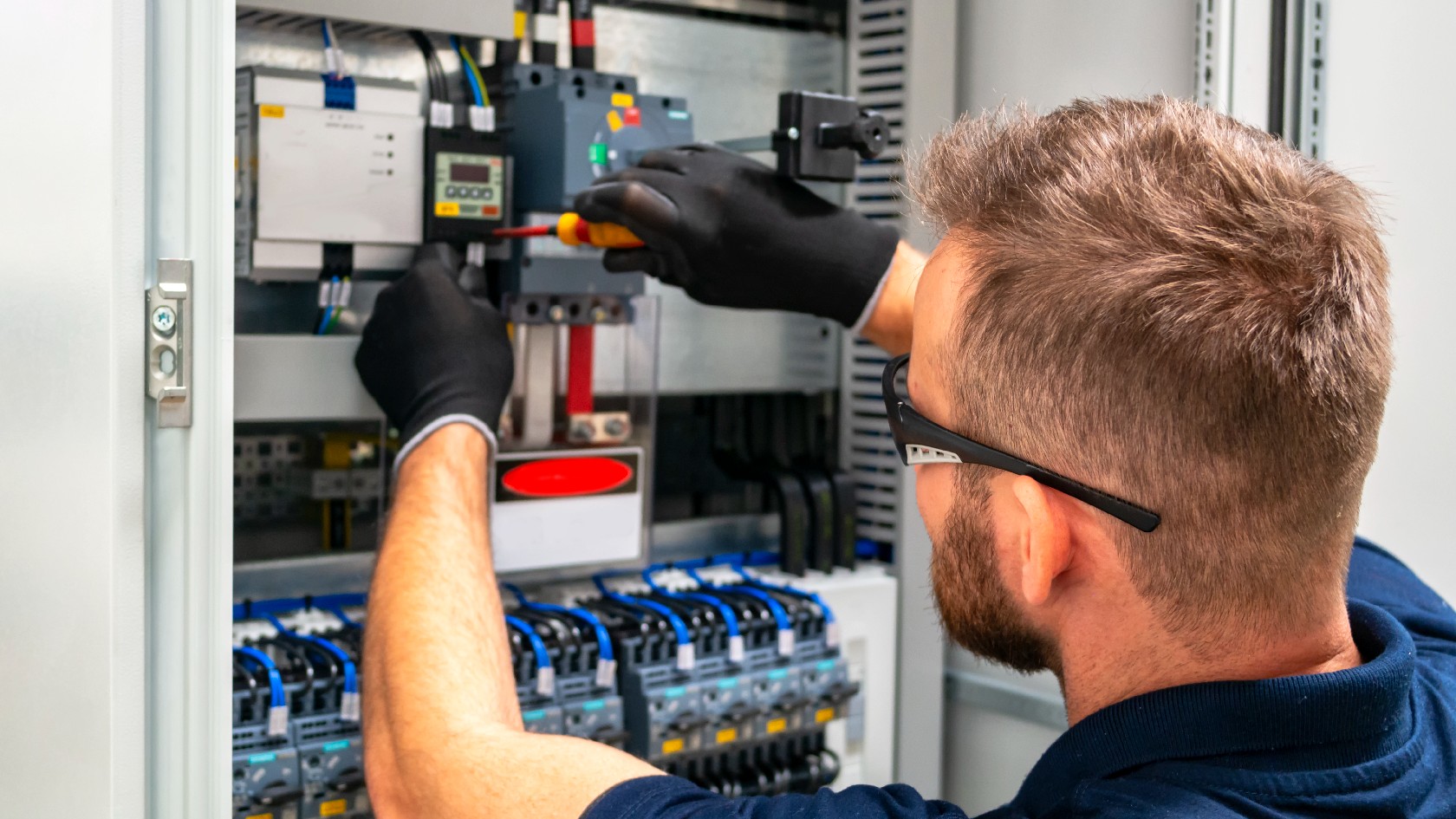 Ein Elektriker mit Schutzbrille und Handschuhen arbeitet an einem Schaltschrank