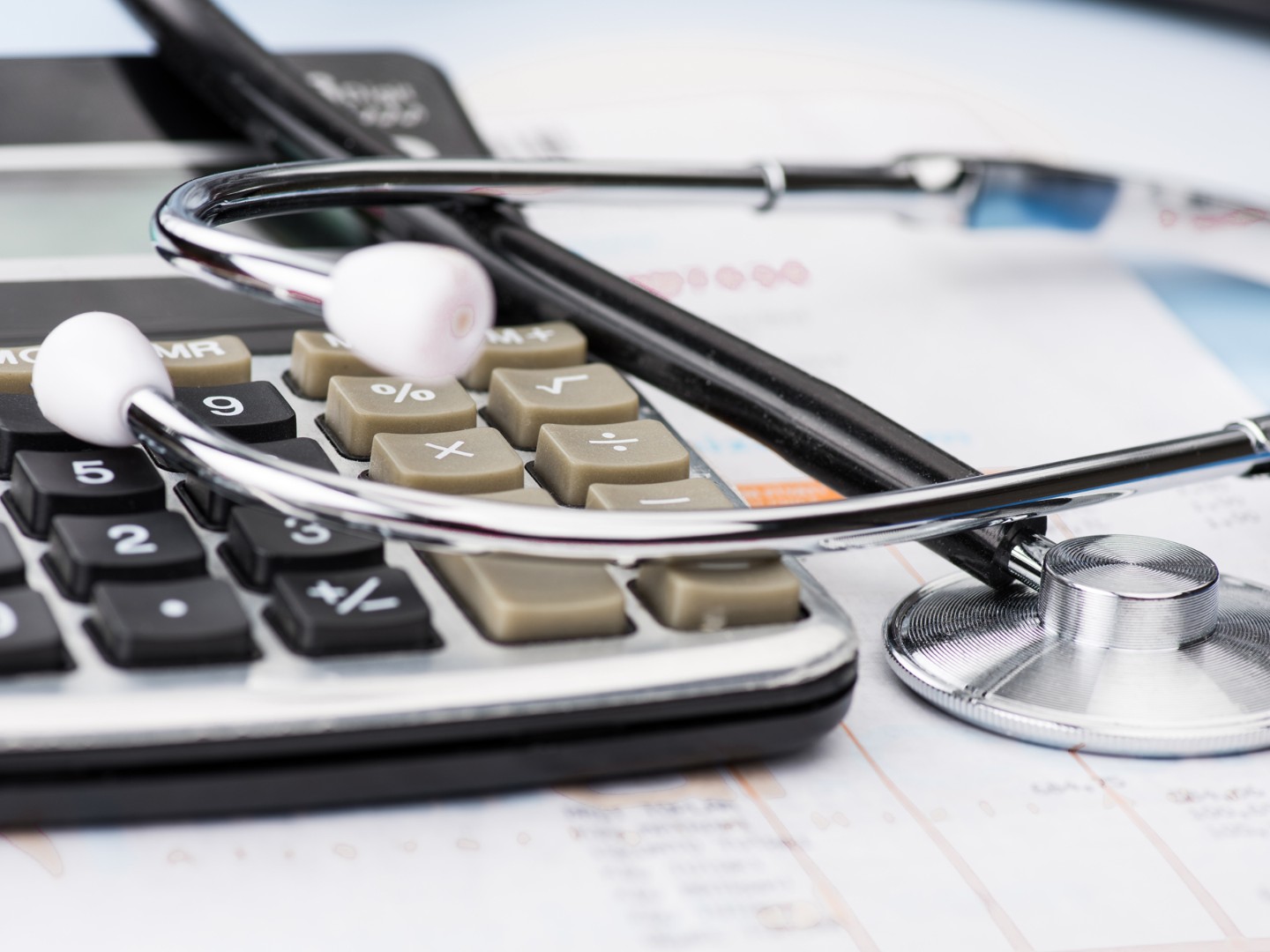 Ein Stethoskop liegt auf einem Taschenrechner und Unterlagen