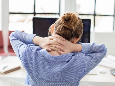 Eine Frau an einem Computerarbeitsplatz hat Nacken- und Rückenschmerzen
