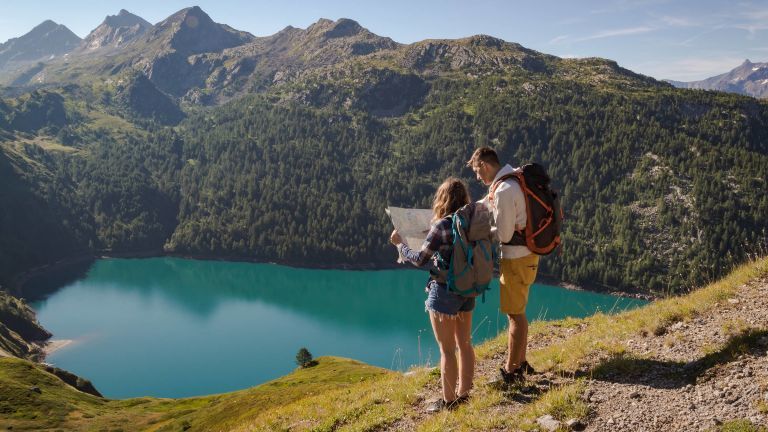 Ein junges Paar steht auf einem Wanderweg und liest eine Karte.