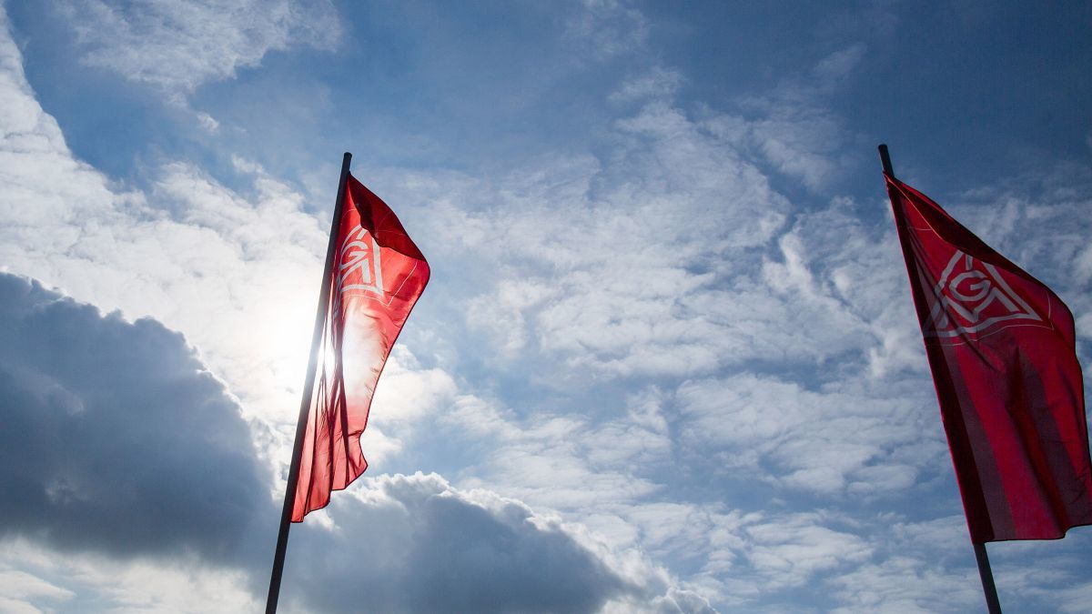 Fahnen der IG Metall vor blauem Himmel mit vereinzelten Wolken.