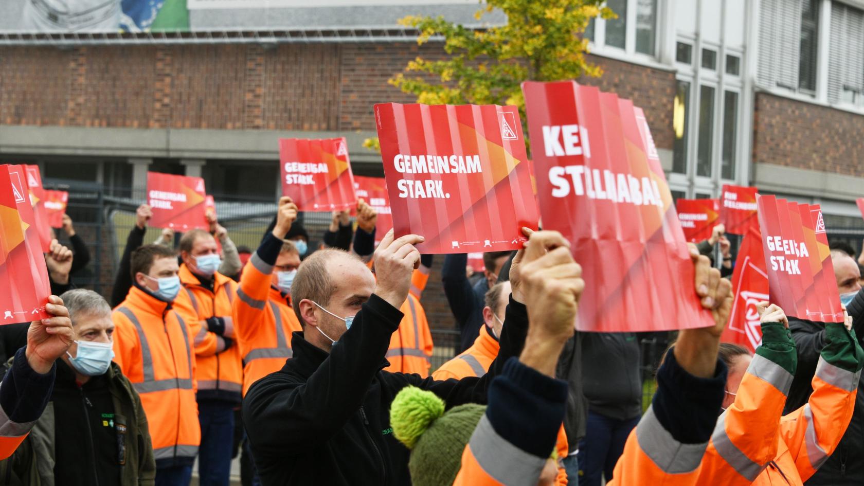 Metaller mit Masken protestieren mit Schildern gegen Stellenabbau