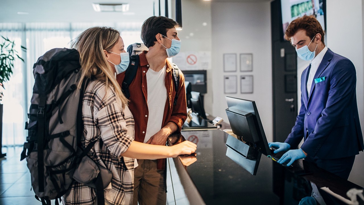 Paar trägt schützende Gesichtsmaske beim Check-in an der Hotelrezeption