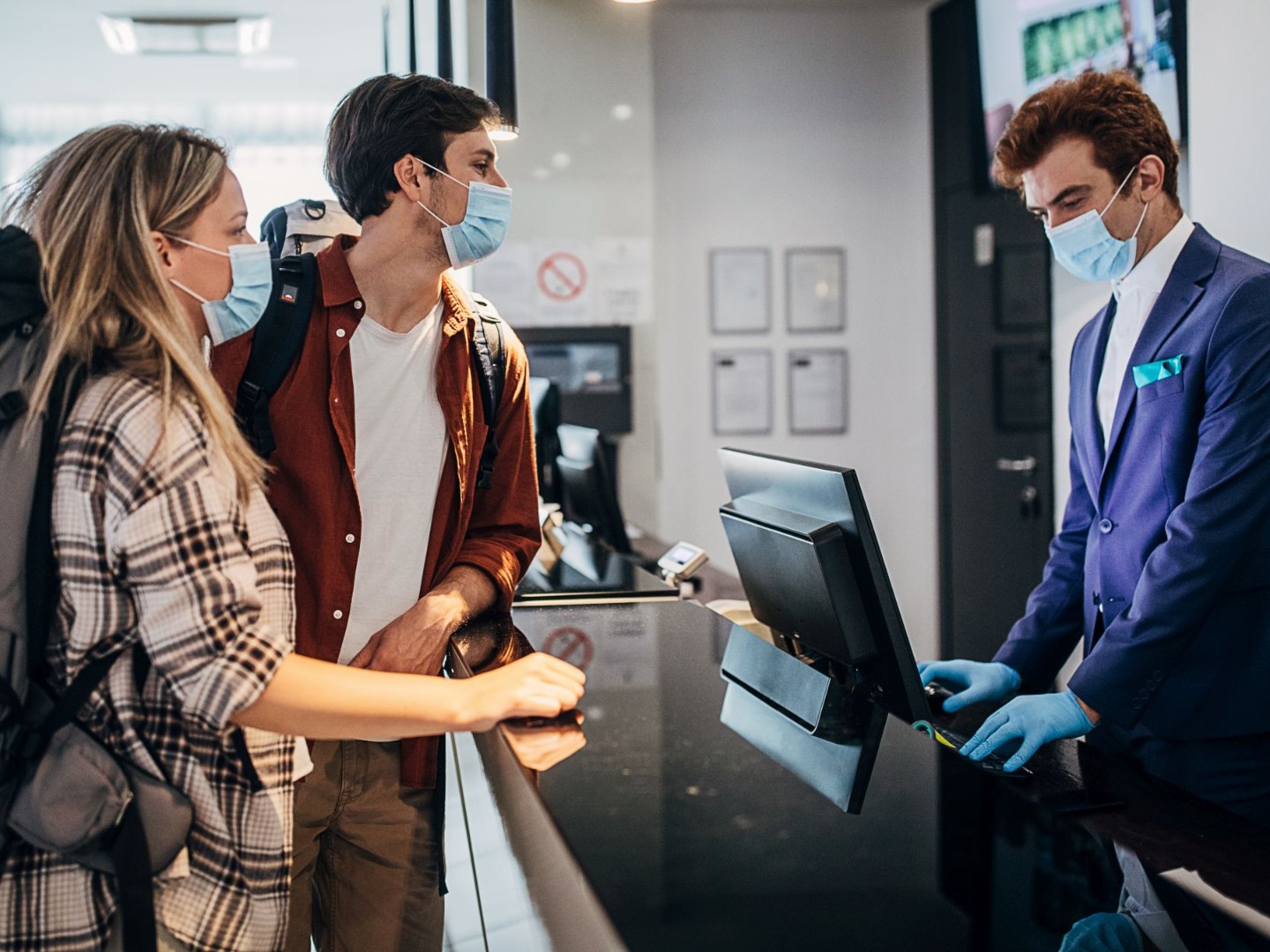 Paar trägt schützende Gesichtsmaske beim Check-in an der Hotelrezeption