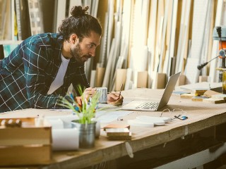 Zimmermann arbeitet in Werkstatt mit Notebook