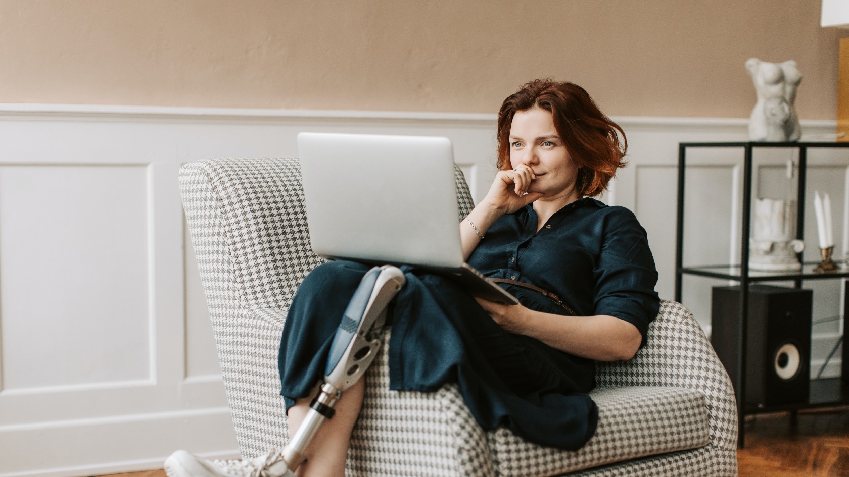 Frau mit Beinprothese lümmelt sich auf  ein Sofa und liest in einem Laptop