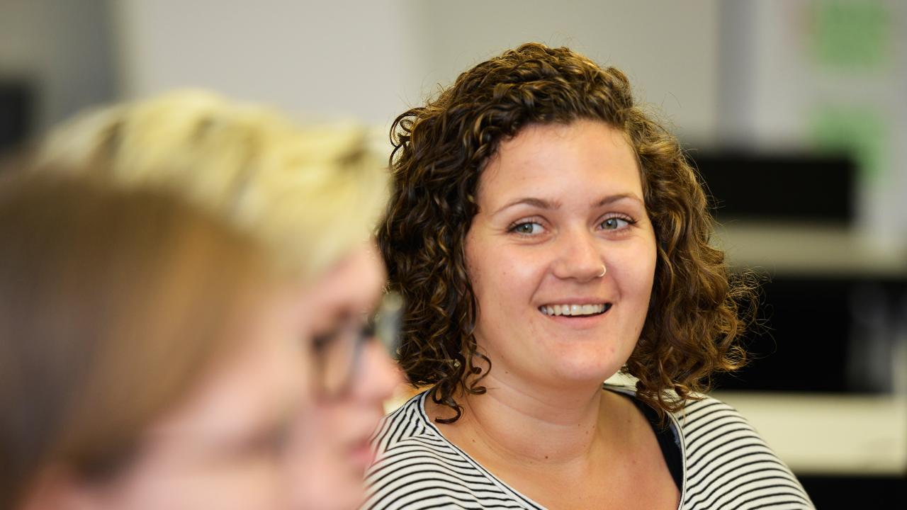 Junge Frau mit Nasenpircing sitzt lächelnd in einem Seminar.